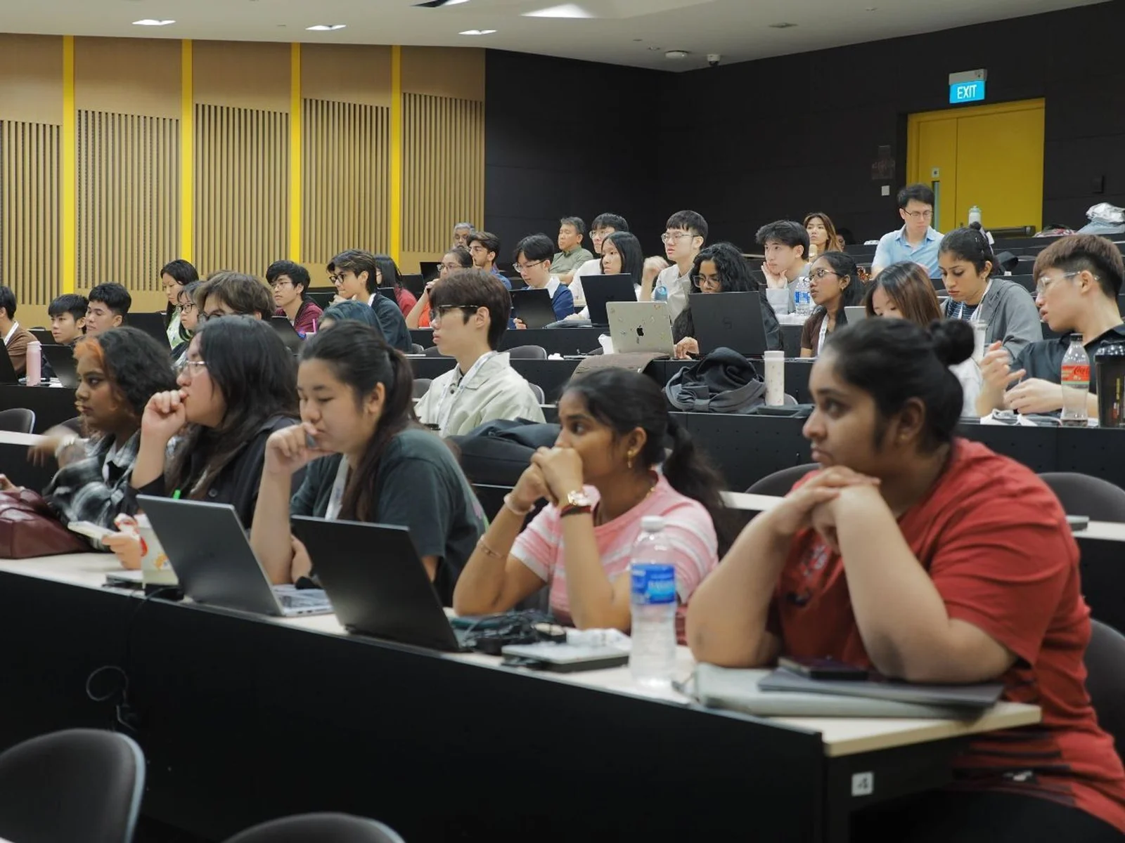 HackXperience 2025 participants working at laptops in a teaching room while a countdown timer is projected behind them